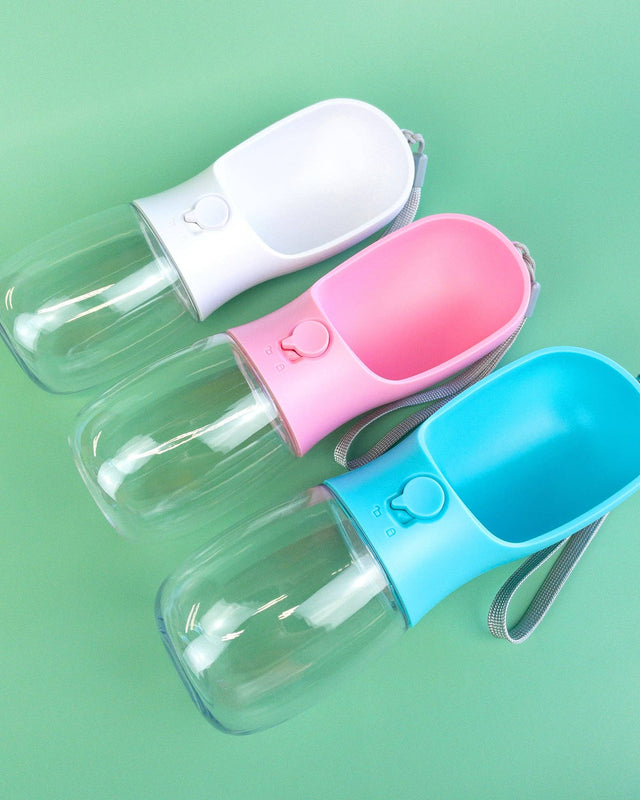 Three portable pet water bottles in white, pink, and blue on a green background.